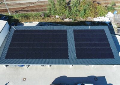 Gewerbe-Carports mit großflächiger Photovoltaikanlage, Trapezblechdach und darunterliegenden Parkplätzen.