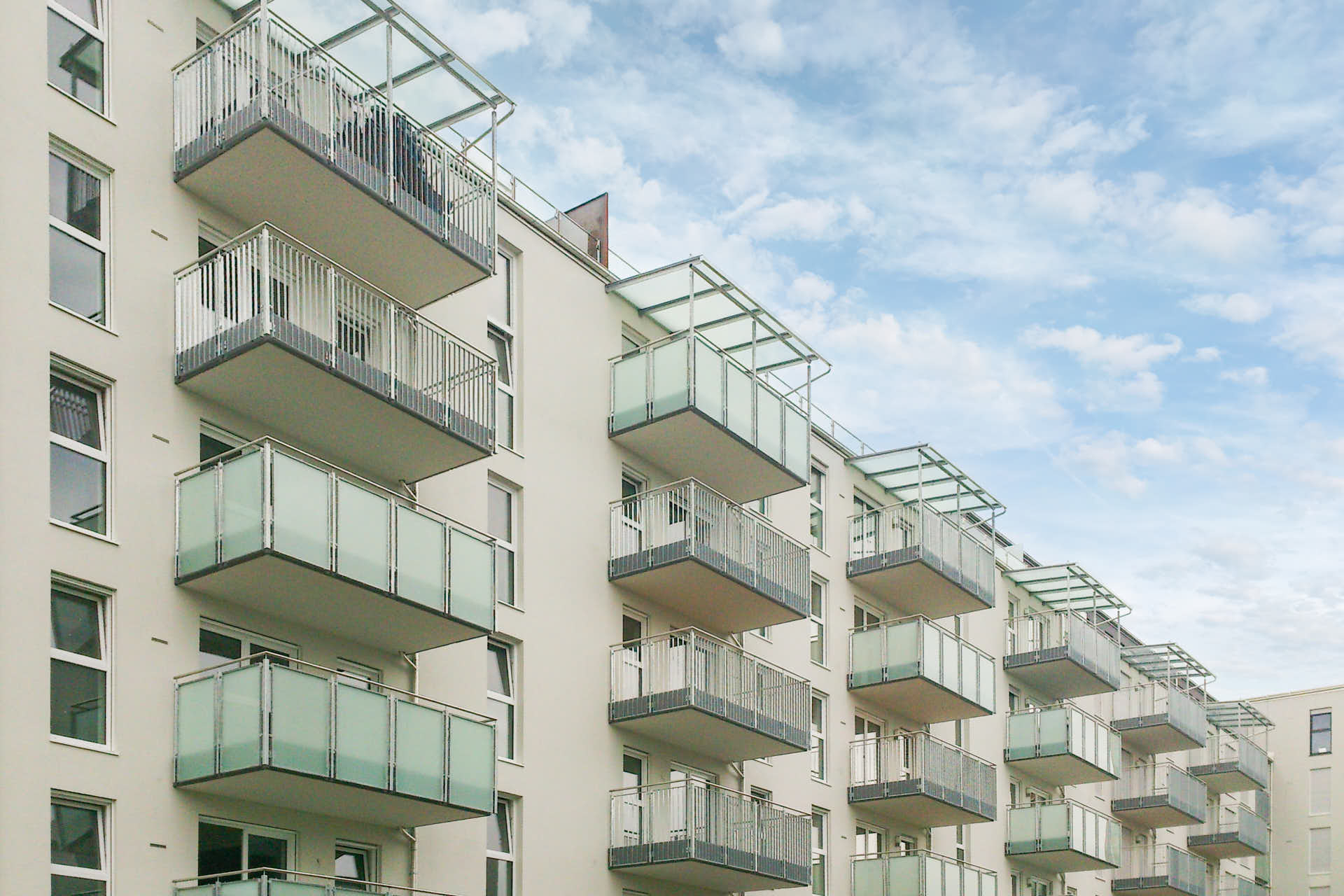 Glasbalkone an einem Mehrfamilienhaus mit teilweise blickdichten Glasbrüstungen und transparenten Überdachungen.