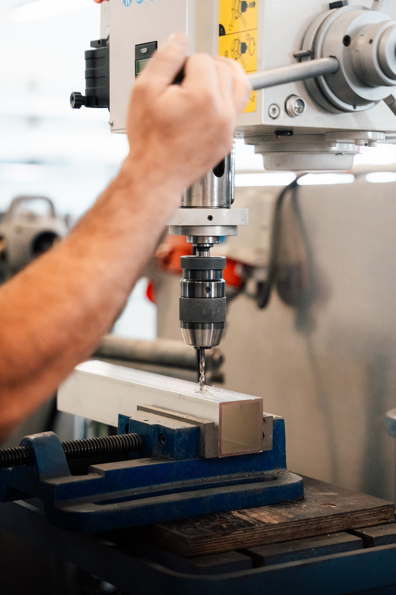 Nahaufnahme eines Mitarbeiters, der ein Metallprofil mit einer Präzisionsbohrmaschine in einer Werkstatt bohrt.