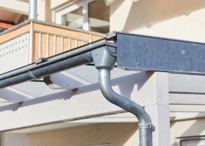Detaillierte Ansicht der Entwässerung eines weißen Holz-Terrassendachs mit verzinktem Ortgangblech und Regenrinne.