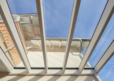 Ansicht von unten auf eine weiße Holz-Terrassenüberdachung mit Glaselementen, die an einer Hauswand befestigt ist.