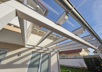 Weiße Holz-Glas-Terrassenüberdachung mit Gebäudeanschluss, bietet hellen, geschützten Außenbereich.
