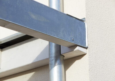 Detailansicht eines verzinkten Traufblechs zum Holzschutz an einem weißen Holzbalken eines Terrassendachs, inklusive Regenrinne.