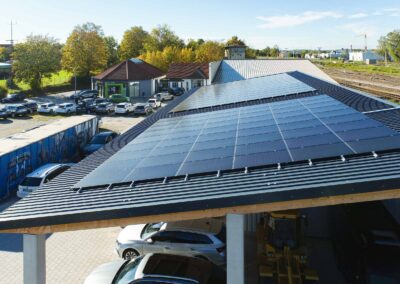 Photovoltaikanlage auf einem gewerblichen Carport mit Pultdach und Trapezblech, darunter parkende Autos eines Autohauses.