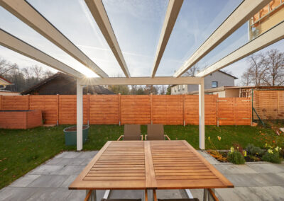 Weißes Holz-Terrassendach mit transparenter Glasüberdachung auf einer gepflasterten Terrasse.