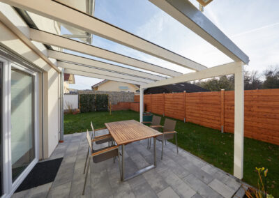 Modernes Terrassendach aus weiß gestrichenem Holz und Glas über einer gepflasterten Terrasse im Garten.