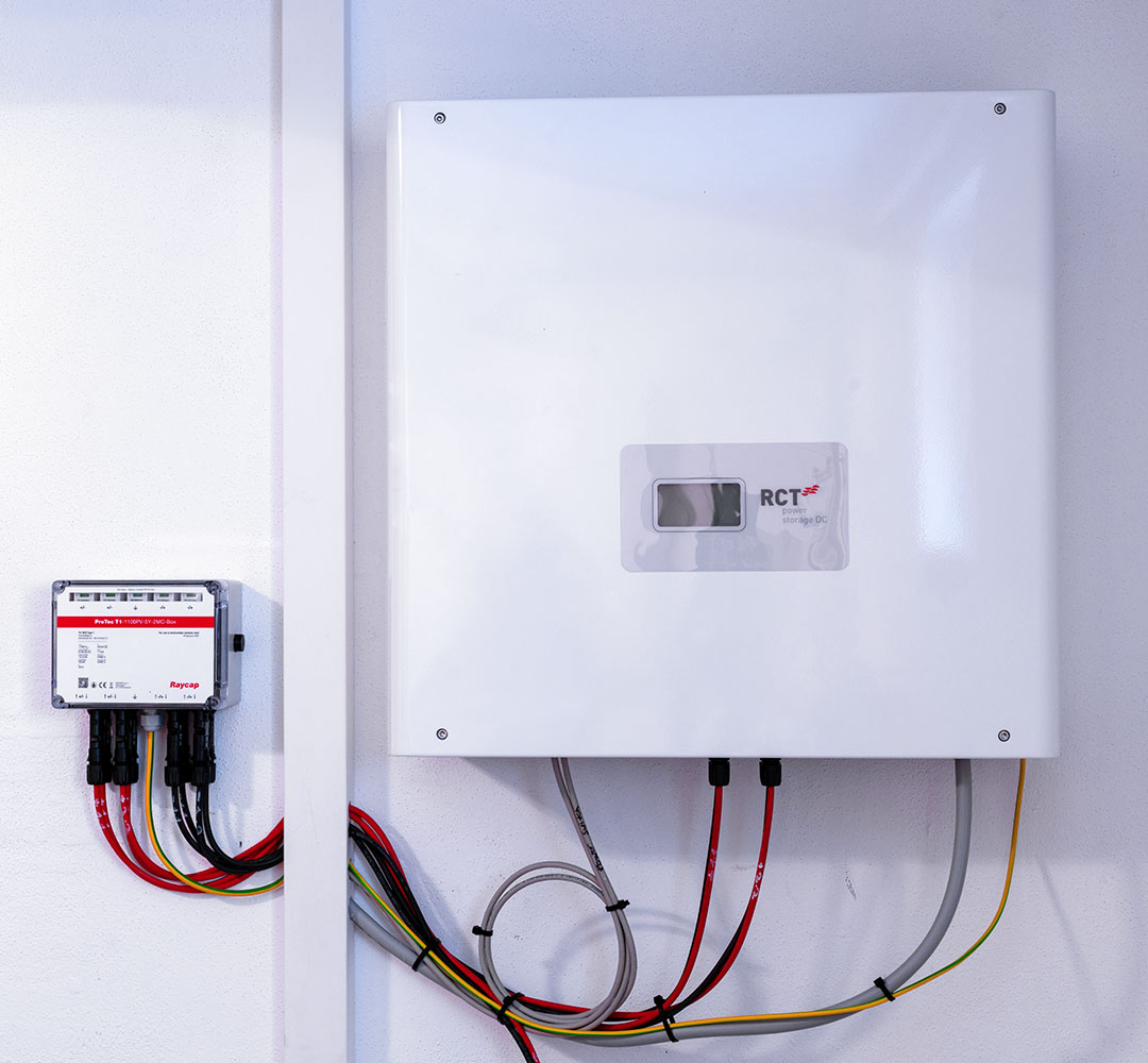 Verkabelter Wechselrichter mit farbigen Anschlussleitungen in einem weißen Gehäuse an der Wand.