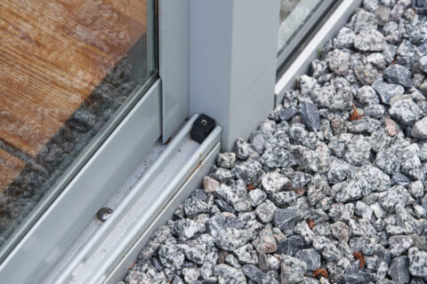 Detail der Aluminium Bodenschiene einer Ganzglasschiebeanlage im Wintergarten mit Holzboden und Zierkies.