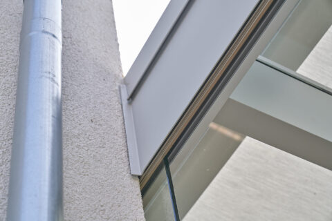 Detaillierte Ansicht des präzisen Wandanschlusses eines Wintergartens an einer Hauswand mit Regenrohr. Maßgefertigte Glasbau…