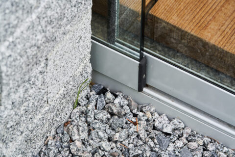 Detailaufnahme des exakten Bodenprofils einer Glasschiebeanlage im Kaltwintergarten, integriert in einen gepflasterten Außen…