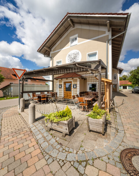 Detailaufnahme der Anschlussstelle eines transparenten Terrassendachs an die Fassade eines Gasthauses mit Außenbestuhlung be…