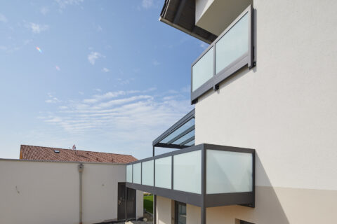 Moderne Balkone mit Glasgeländer und Balkonüberdachung an einem Einfamilienhaus in Dorfen unter blauem Himmel.