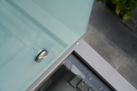 Detailansicht eines modernen Balkongeländers aus mattiertem Glas und gebürstetem Edelstahl, fachmännisch montiert an einem K…