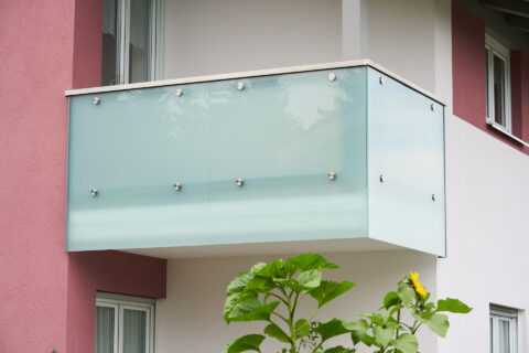 Maßgefertigtes Balkongeländer aus satiniertem Glas und Edelstahl an moderner Hausfassade.