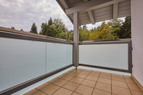 Modernes Balkongeländer aus satiniertem Glas und Metall, montiert von einem Profi in Kolbermoor. Blick auf Baumlandschaft.