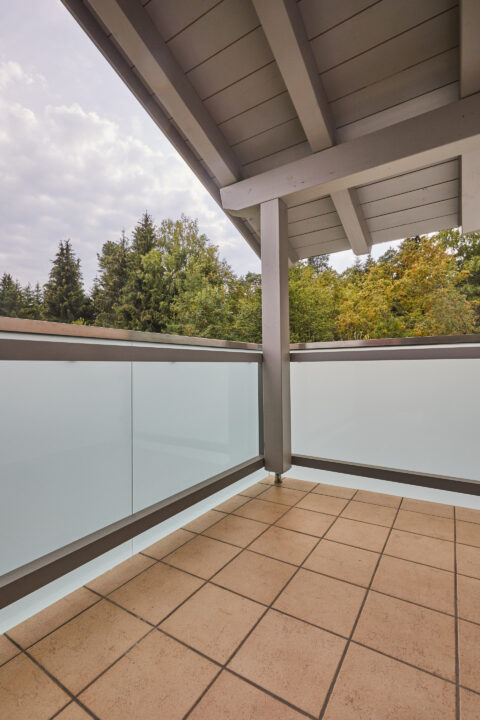 Moderner, verglaster Balkon mit Milchglasgeländer und Holzdecke in Kolbermoor. Perfekt als Kaltwintergarten oder Windschutz.