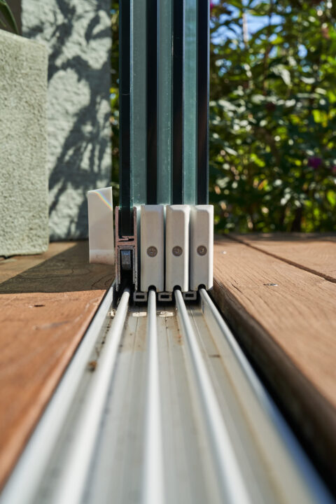 Detailansicht einer barrierefreien Aluminium-Schiebeanlage, nahtlos in Terrassenholz integriert, für Kaltwintergarten.