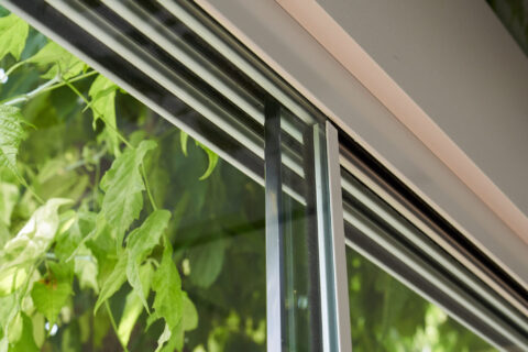Close-up of a multi-track sliding glass system with aluminum rails, visible against a green garden background, demonstrating…