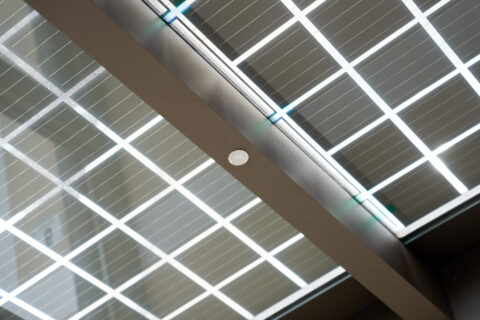 Detailaufnahme einer modernen Terrassenüberdachung mit integrierten Solarmodulen und einem Einbaustrahler in der tragenden S…