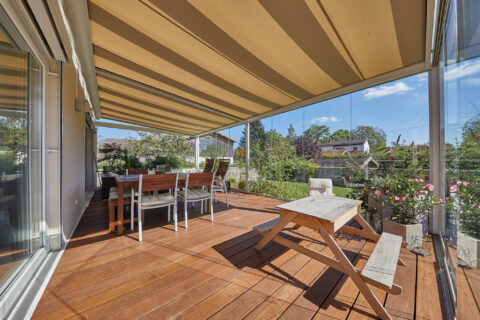Sottezza Unterdachbeschattung in einem Kaltwintergarten mit Glasdach, Holzboden und Essbereich, umgeben von Garten.