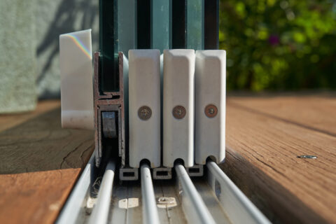 Detailansicht der Bodenschiene einer Sunparadise Schiebeanlage für einen Kaltwintergarten mit Glaspaneelen und Holzterrasse.