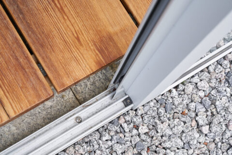 Nahaufnahme der robusten Bodenschiene eines Glasschiebesystems für Terrassenüberdachungen, nahtlos integriert mit Holzterras…