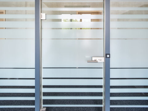 Modernes Glastürelement mit Milchglasstreifen und elegantem Drücker für Büroräume, bietet Privatsphäre und Licht.