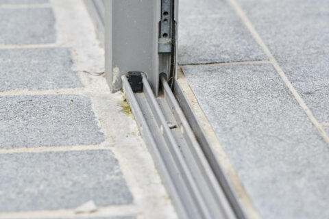Detailansicht einer ebenerdigen Bodenschiene für eine Schiebeanlage, nahtlos in graue Pflastersteine integriert.