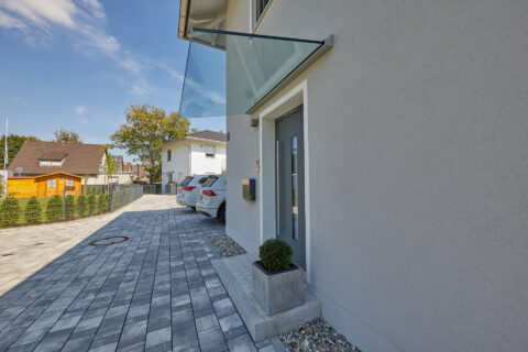 Freitragende Glasüberdachung am modernen Hauseingang, schützt die graue Haustür vor Regen.