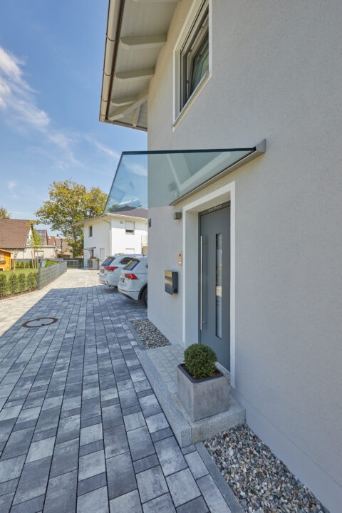 Ganzglas-Eingangsüberdachung am modernen Hauseingang schützt vor Witterung.