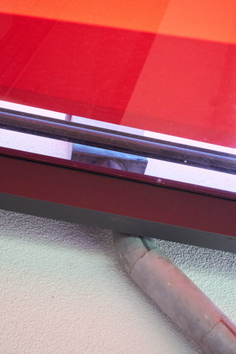 Detailansicht der integrierten Fallrohr-Entwässerung im Seitenbereich einer Aluminium-Terrassenüberdachung mit roter Markise.