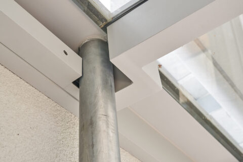 Detailansicht eines elegant in ein Terrassendach aus Aluminium und Glas integrierten Fallrohrs für effektive Wasserableitung.