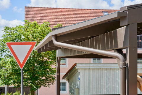 Braune Fallrohrverlängerung und Regenrinne an einem modernen Terrassendach aus Glasbau in Niederbergkirchen, detailreich.