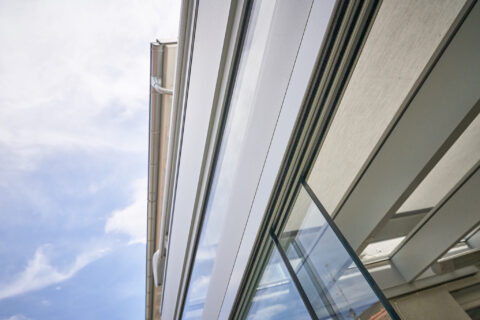 Moderner Wintergarten mit filigraner Aluminiumkonstruktion, Glasdach und integriertem Sonnenschutz vor blauem Himmel.