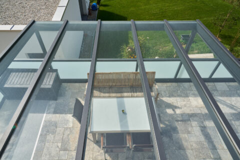 Filigranes Klarglas-Terrassendach installiert über einer modernen Terrasse mit Outdoor-Möbeln und Fliesenboden in Dorfen.