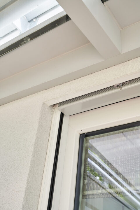 Detailansicht des oberen Anschlussbereichs eines Kaltwintergartens an einen Balkon mit Firstpfette und Rollladenkasten in Zo…