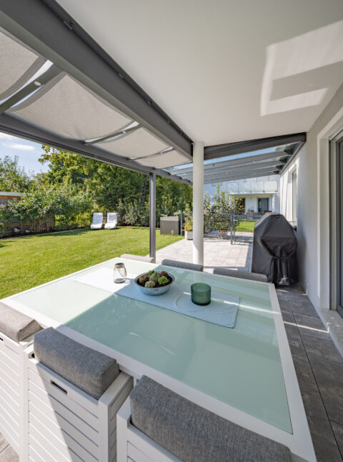 Terrassenüberdachung mit integriertem Sonnenschutz und moderner Outdoor-Möbelgruppe als Freisitz.