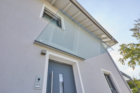 Freitragendes Glasvordach über modernem Hauseingang, schützt vor Witterung und integriert sich minimalistisch in die Fassade.