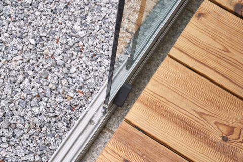 Detail der bodenbündigen Ganzglasschiebeanlage Sunparadise mit versenkter Führungsschiene und Holzdielen.