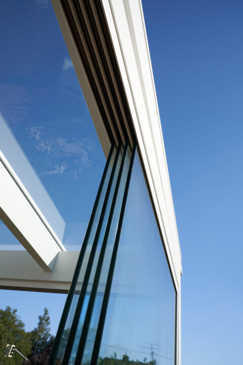 Detailansicht eines modernen Kaltwintergartens mit transparenten Ganzglasschiebeelementen von Sunparadise VG 15 unter blauem…