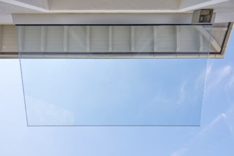 Ganzglasvordach Canopy an Hausfassade mit blauem Himmel im Hintergrund, für modernen Wetterschutz.