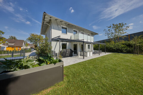Modernes Einfamilienhaus mit eleganter Glas-Terrassenüberdachung und angrenzendem Garten in Feldkirchen.
