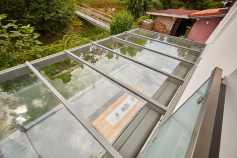 Geschlossene Glas-Terrassenüberdachung mit Aluminiumrahmen an einem Einfamilienhaus in grüner Umgebung bei Kolbermoor.