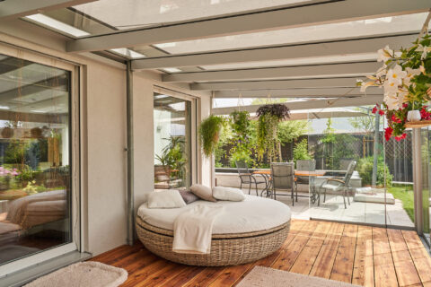 Moderne Glas-Terrassenüberdachung mit komfortabler Outdoor-Lounge, Holzboden und Blick auf den gepflegten Gartenbereich.