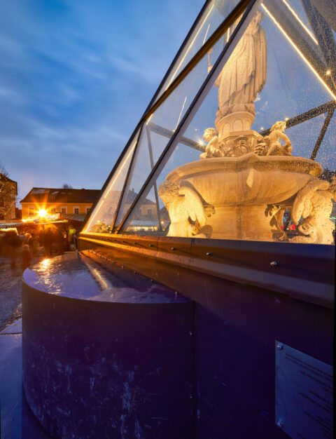 Marienbrunnen in Altötting unter eleganter Glas-Einhausung bei Abenddämmerung.
