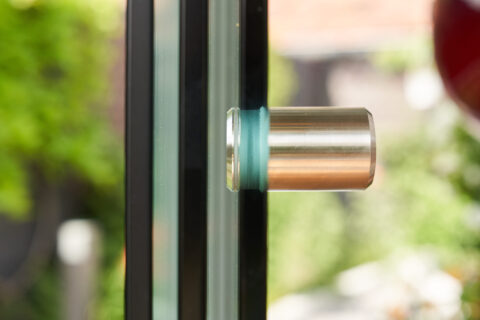 Nahaufnahme eines modernen Glas-Schiebeelements mit elegantem Edelstahlgriff und Mehrfachverglasung, ideal für Terrassenüber…