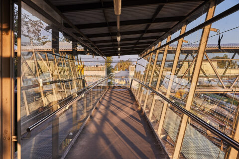 Glasüberführung zwischen Parkhaus und Bahnhof Mühldorf am Inn, mit Sonnenlicht und Reflektionen, sicherer und heller Übergan…