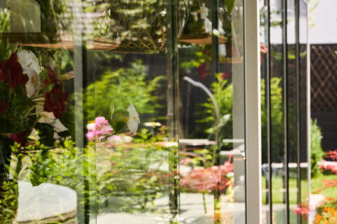 Moderner Glaswintergarten in Zorneding mit transparenter Fassade, die einen üppigen Garten reflektiert.