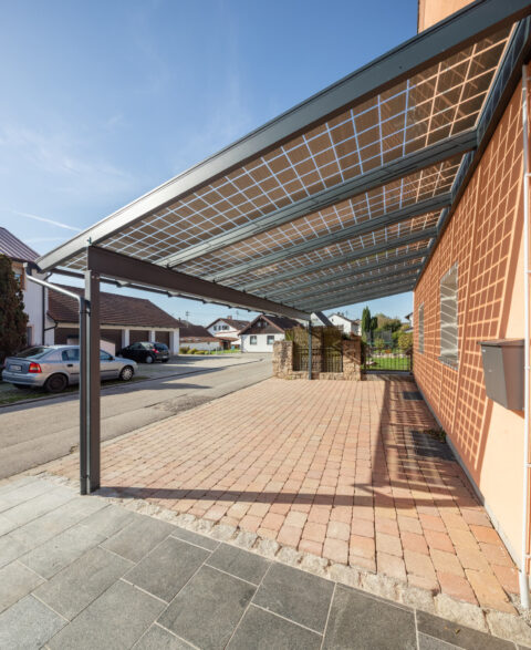 Großer PV-Carport mit Pultdach als eleganter Hausanbau, spendet Schatten und erzeugt Solarstrom auf der Einfahrt eines Eigen…