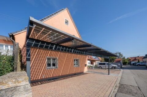 Großer, moderner Photovoltaik-Carport an einem Einfamilienhaus in Mühldorf am Inn bei strahlendem Sonnenschein.